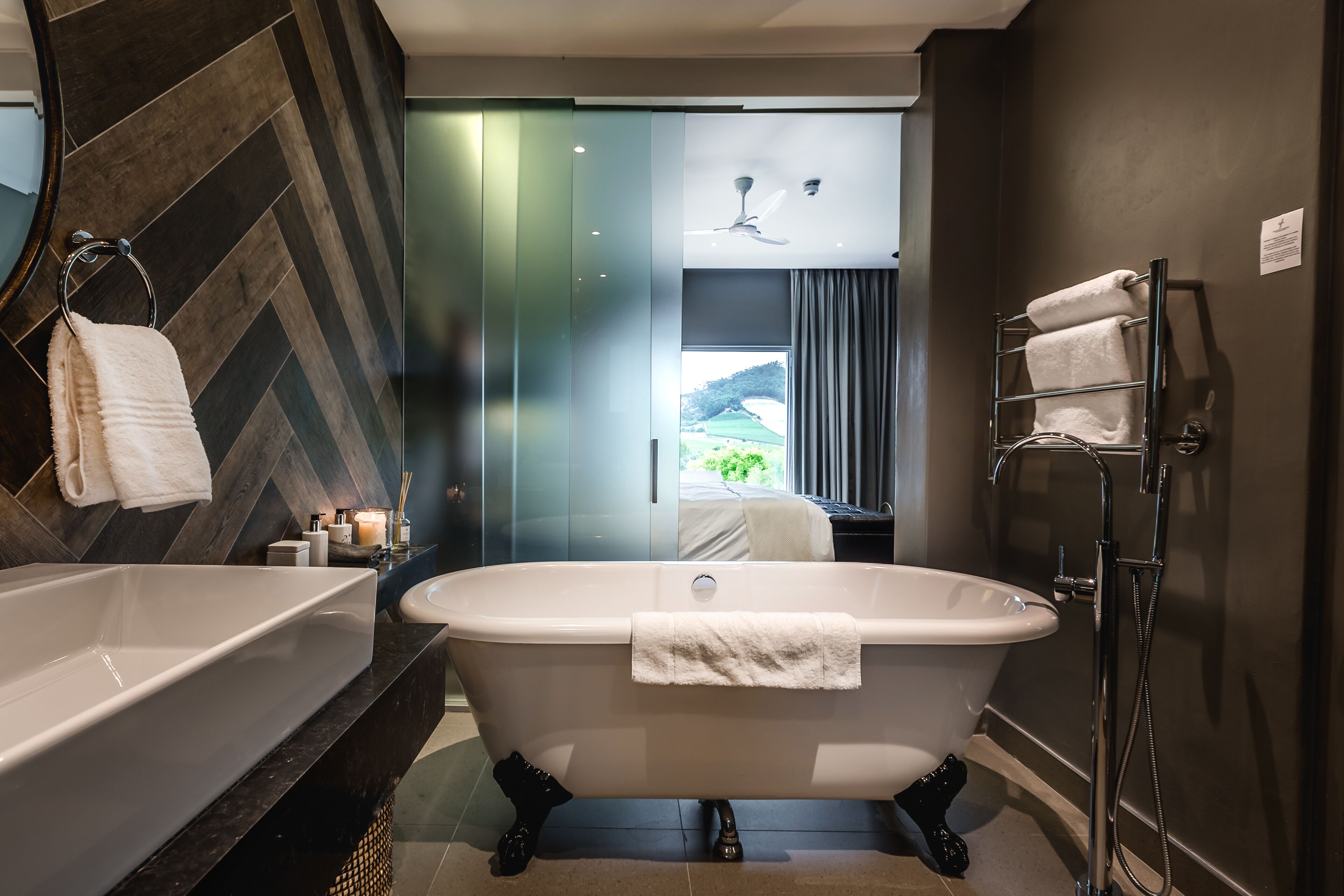 A modern bathroom with a freestanding bathtub, a glass shower enclosure, and a view of a green landscape through the window.