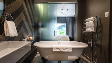 A modern bathroom with a freestanding bathtub, a glass shower enclosure, and a view of a green landscape through the window.