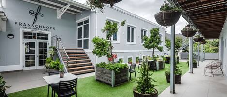 A boutique hotel with a reception area, outdoor seating, and a garden with planters and a staircase.