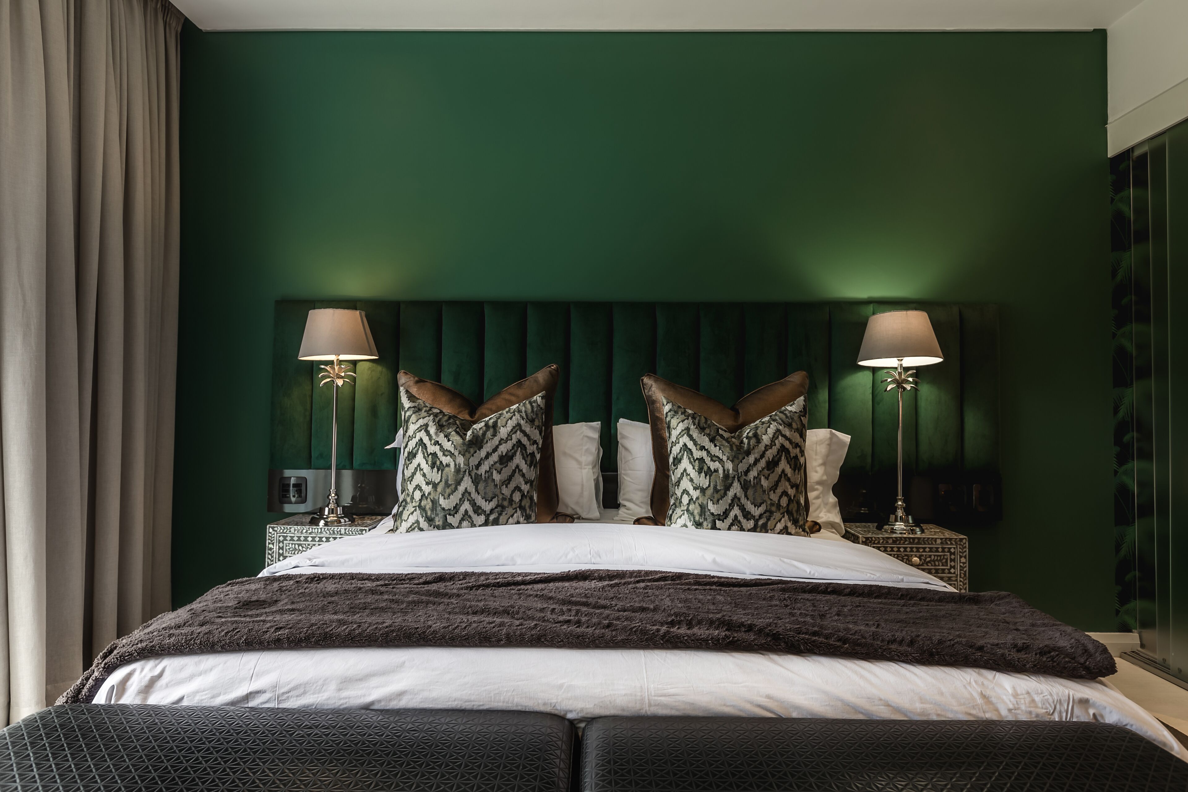 A bed with a dark headboard, two bedside lamps, and patterned pillows.
