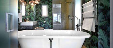 Un baño moderno con una bañera independiente, cabina de ducha con mampara de vidrio y un perchero con varias toallas.