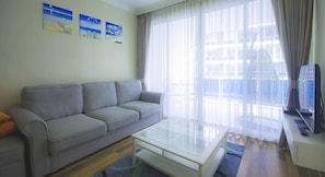 A living room with a grey sofa, a glass coffee table, and a television on a stand.