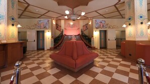 A lobby with a checkered floor, a central red sofa, and a staircase with a pink railing.
