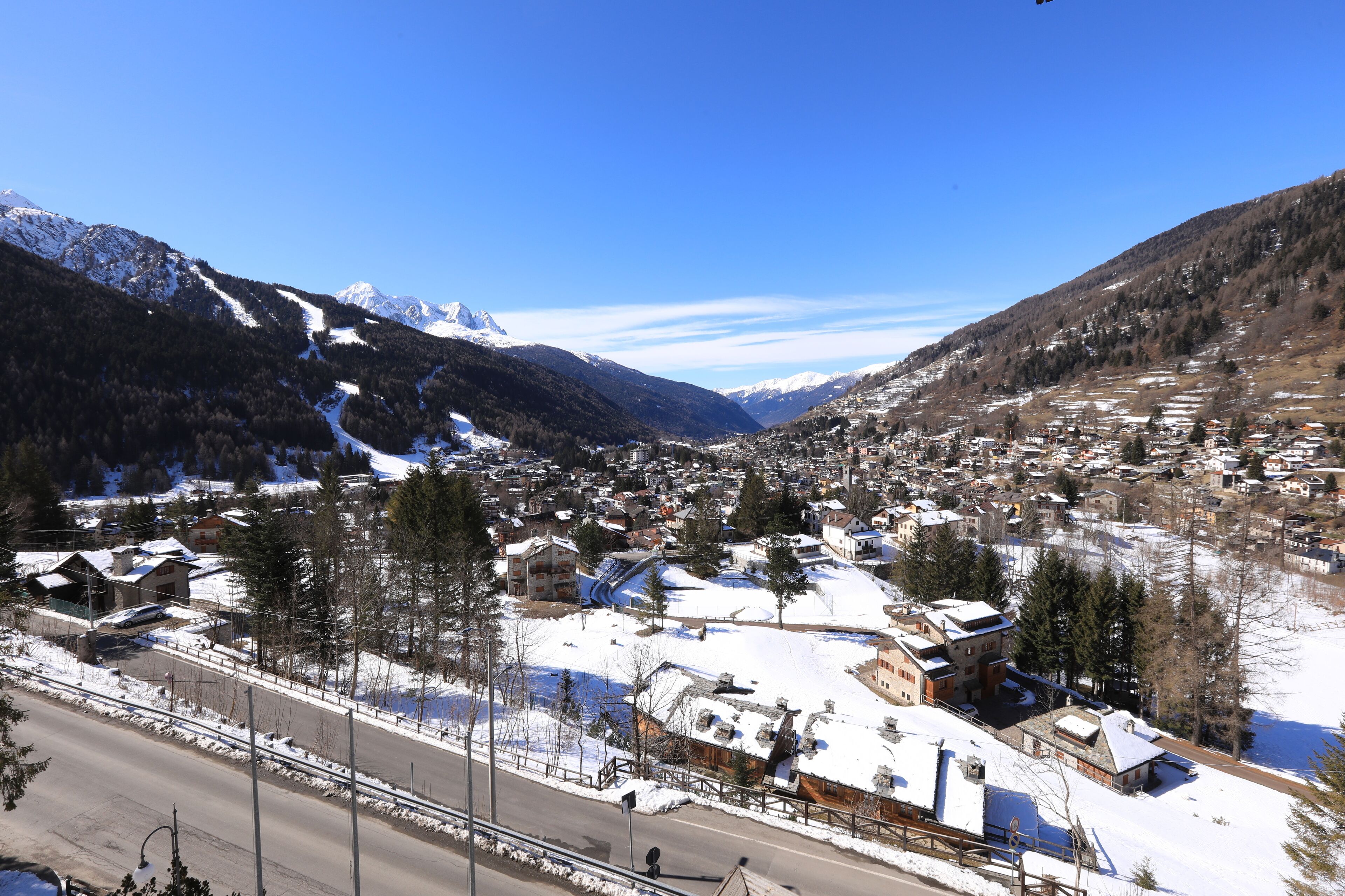 A snow-covered town with buildings, a road, and mountains in the background.
