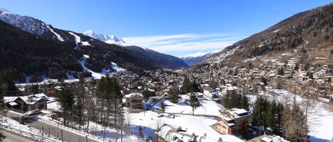 A snow-covered town with buildings, a road, and mountains in the background.
