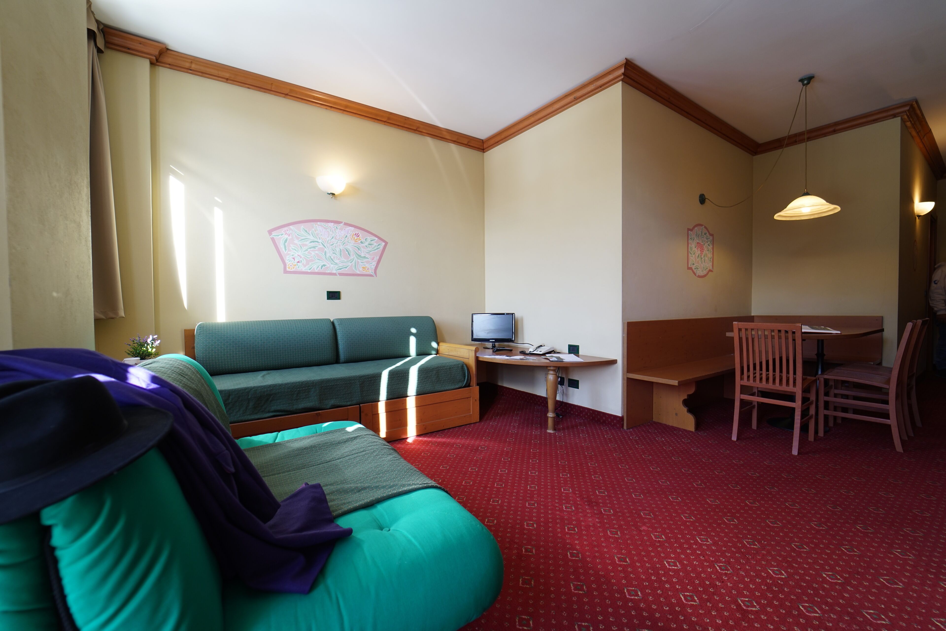 Ein Zimmer mit einem grünen Sofa, einem kleinen Schreibtisch mit einem Computer, einem Stuhl und einem roten Teppich mit Muster.
