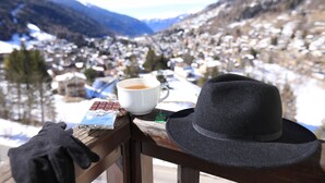 A wooden railing with a black hat, a white mug with a tea bag, and a chocolate bar.