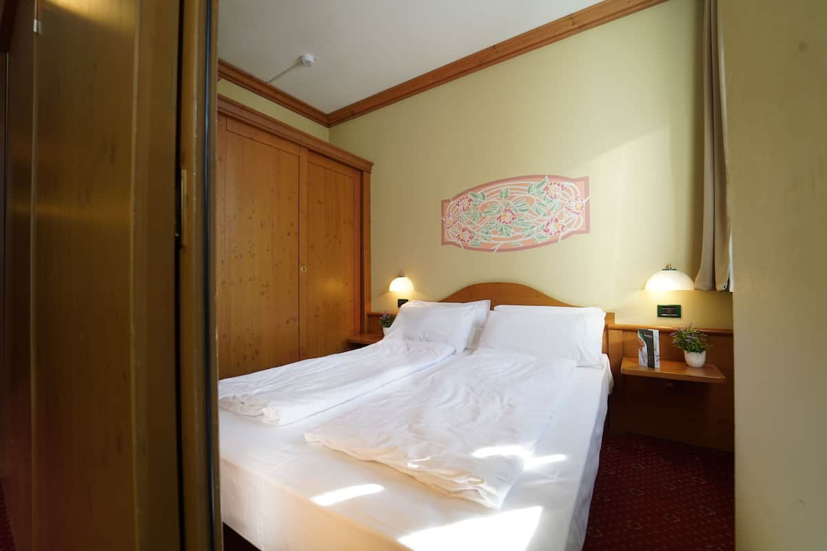 Une chambre d’hôtel avec une armoire en bois, un lit avec du linge de maison blanc, un élément décoratif mural et deux lampes de chevet.