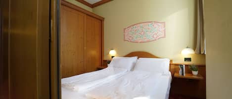 Habitación de hotel con un armario de madera, una cama con ropa blanca, un adorno en la pared y dos lámparas de noche.