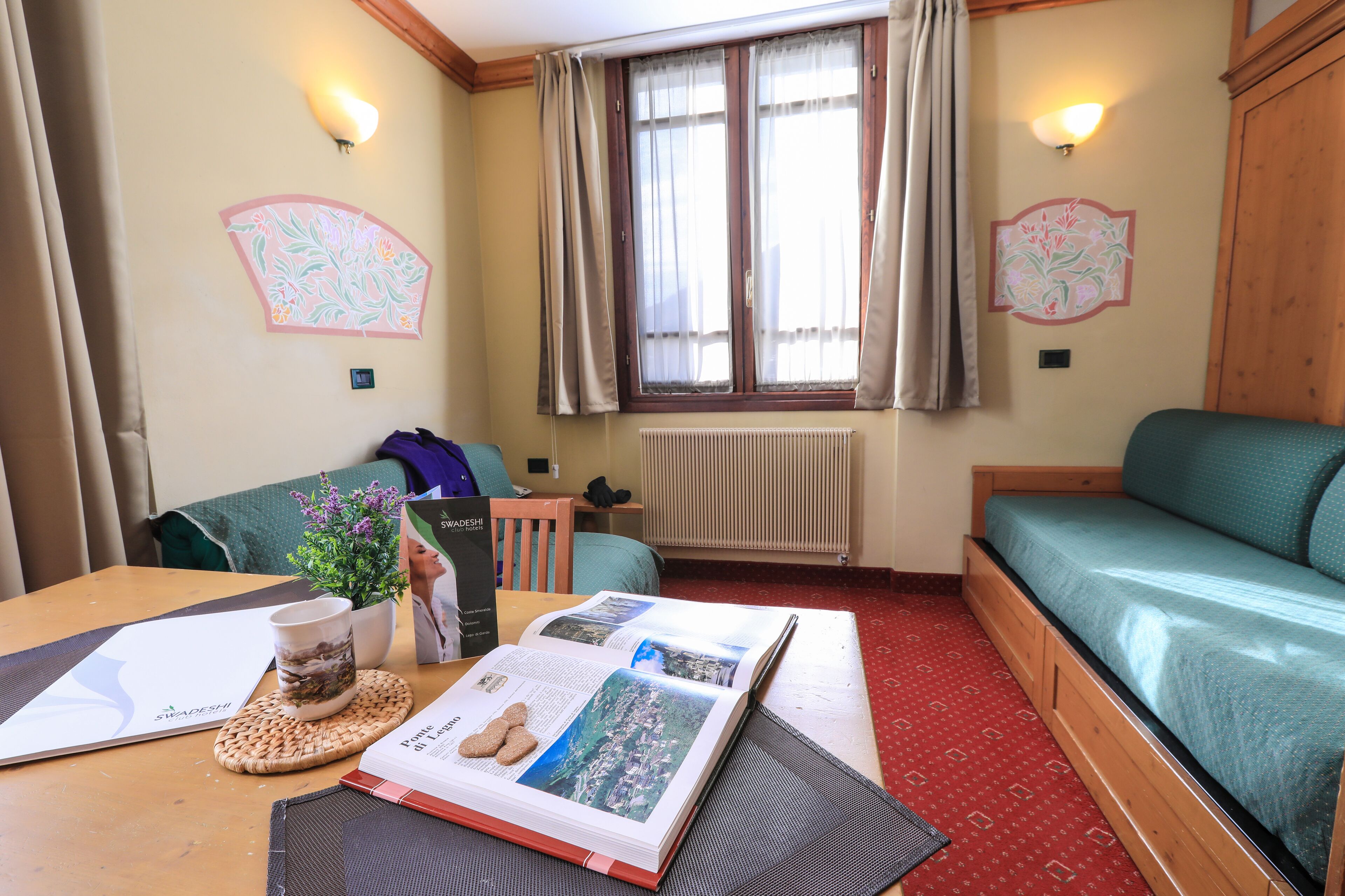 A cozy room with a wooden table, a green sofa, a small plant, and a book.