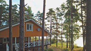 A cabin with a wooden exterior, a covered porch, and a view of the surrounding forest. - Villa Helga (Kemiönsaari)