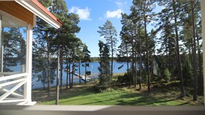 A view from a window overlooking a lake surrounded by tall trees and a wooden deck. - Villa Helga (Kemiönsaari)