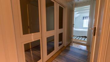 Un pasillo con suelo de madera y paredes blancas que conduce a un dormitorio con cama y ventana.