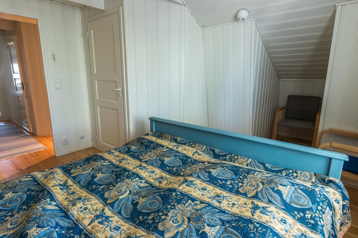 A bedroom with a bed, a door, and a chair.