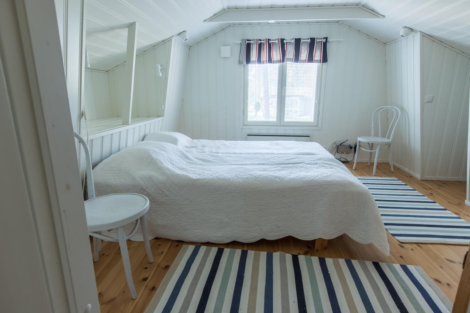 A bedroom with a bed, a chair, a window with curtains, and a striped rug.