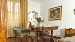 Una habitación con una mesa de madera, dos sillas, una cama, un espejo y un cuadro en la pared.