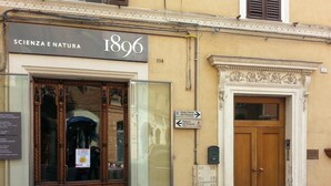 Fachada de edificio con un cartel que dice "SCIENZA E NATURA 1896" y una puerta con un panel de vidrio.