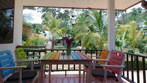 Un espace extérieur abrité, aménagé avec une table en bois et des chaises colorées, entouré d’une végétation tropicale luxuriante.