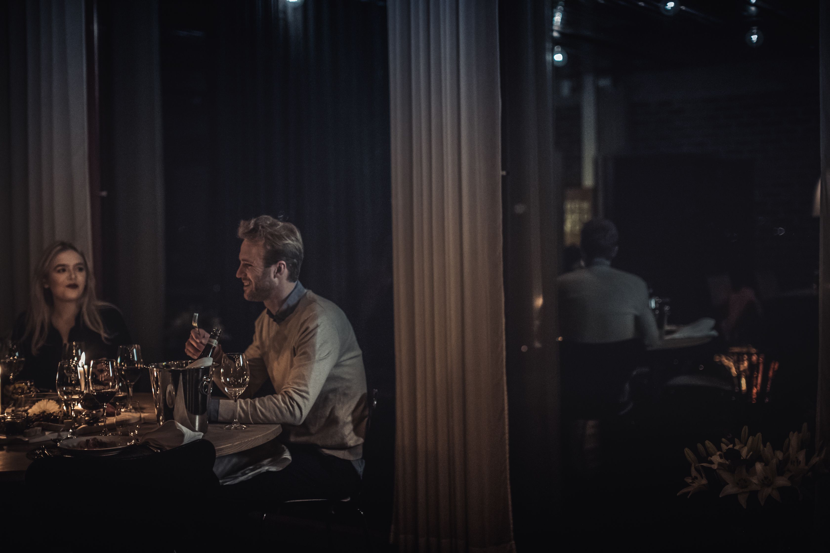A dimly lit restaurant with a table set for two, featuring a wine glass, a bottle, and a menu.
