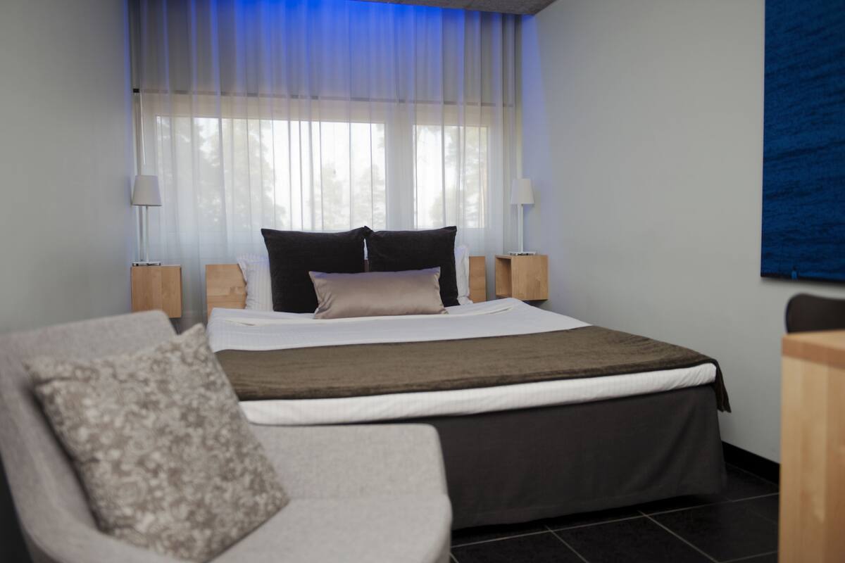 A modern bedroom with a large bed, two bedside tables, a chair, and a window with sheer curtains.