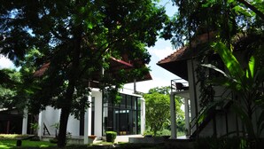 A modern building with large glass windows, surrounded by lush greenery and trees. - BAAN 88 Chiang Mai (Mae Rim)