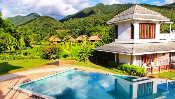A resort with a large swimming pool, a thatched-roof building, and lush greenery in the background. - Pai Vieng Fah (Pai)