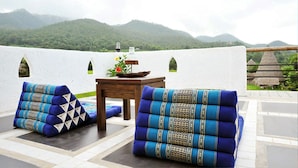 A terrace with a table and chairs, a flower arrangement, and a view of green hills. - Pai Vieng Fah (Pai)