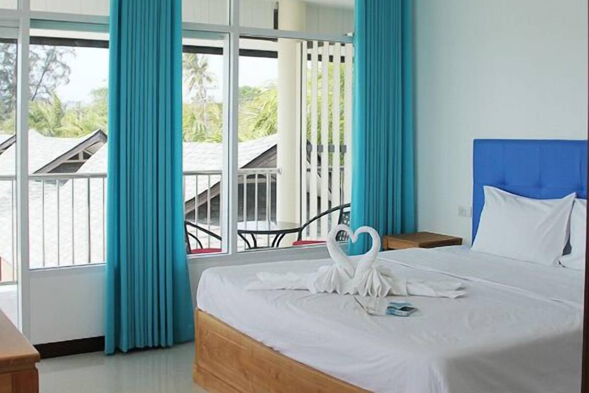 Une chambre d’hôtel avec un lit, une tête de lit en bois, un balcon avec une balustrade et une vue sur la verdure environnante.