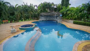 Une piscine agrémentée d’une cascade, entourée d’une végétation luxuriante et dotée d’une terrasse en bois.