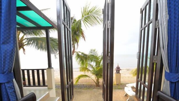 Une terrasse en bois ouverte, donnant sur une plage bordée de palmiers et sur laquelle se trouve une petite construction.