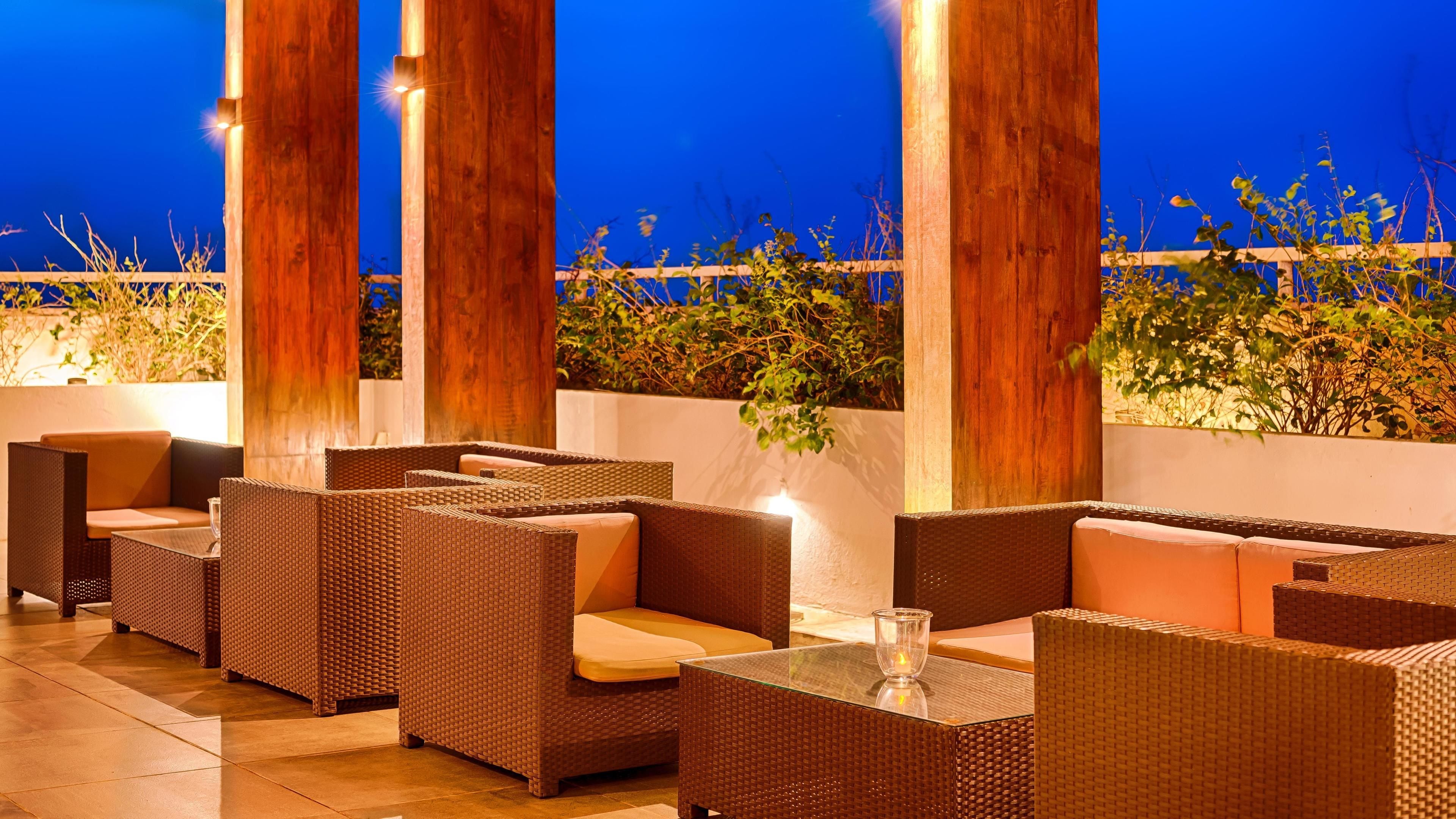A rooftop patio with wicker furniture, a glass table, and a view of the night sky.
