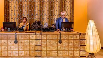A reception desk with two monitors, a traditional lamp, and a decorative metal wall.