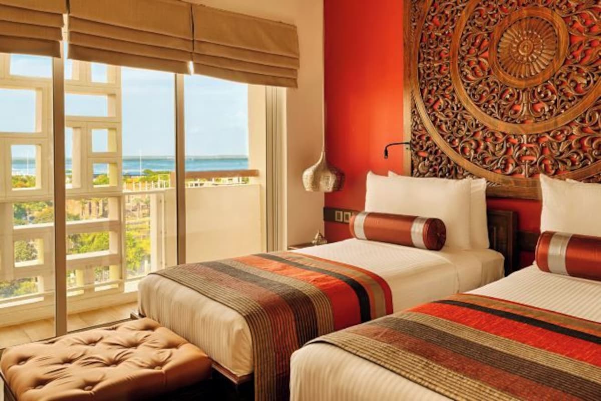 A hotel room with two beds, a large window with a view of the ocean, and a decorative wall panel.