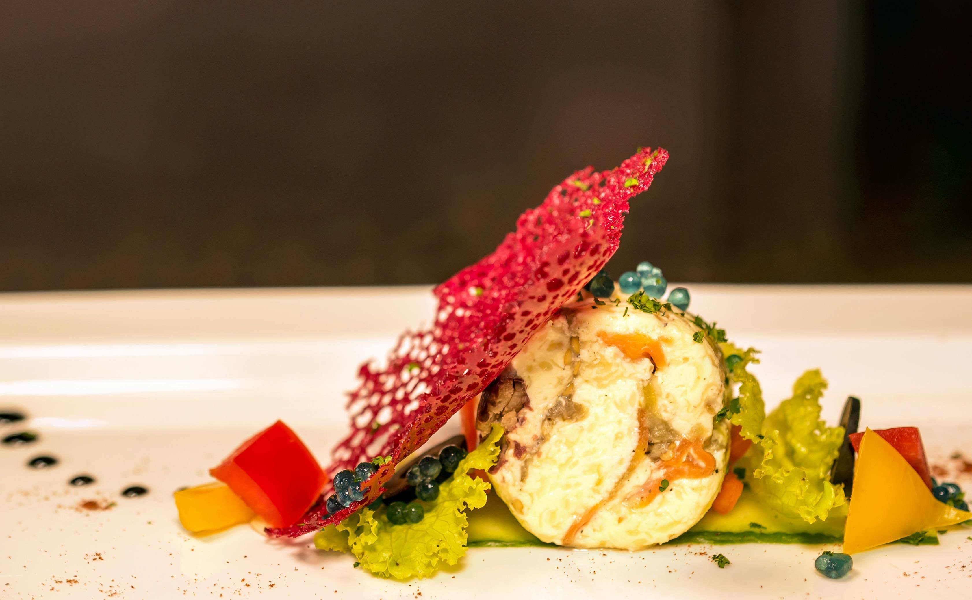 A dish with a red edible net, green lettuce, and a yellow element on a white plate.