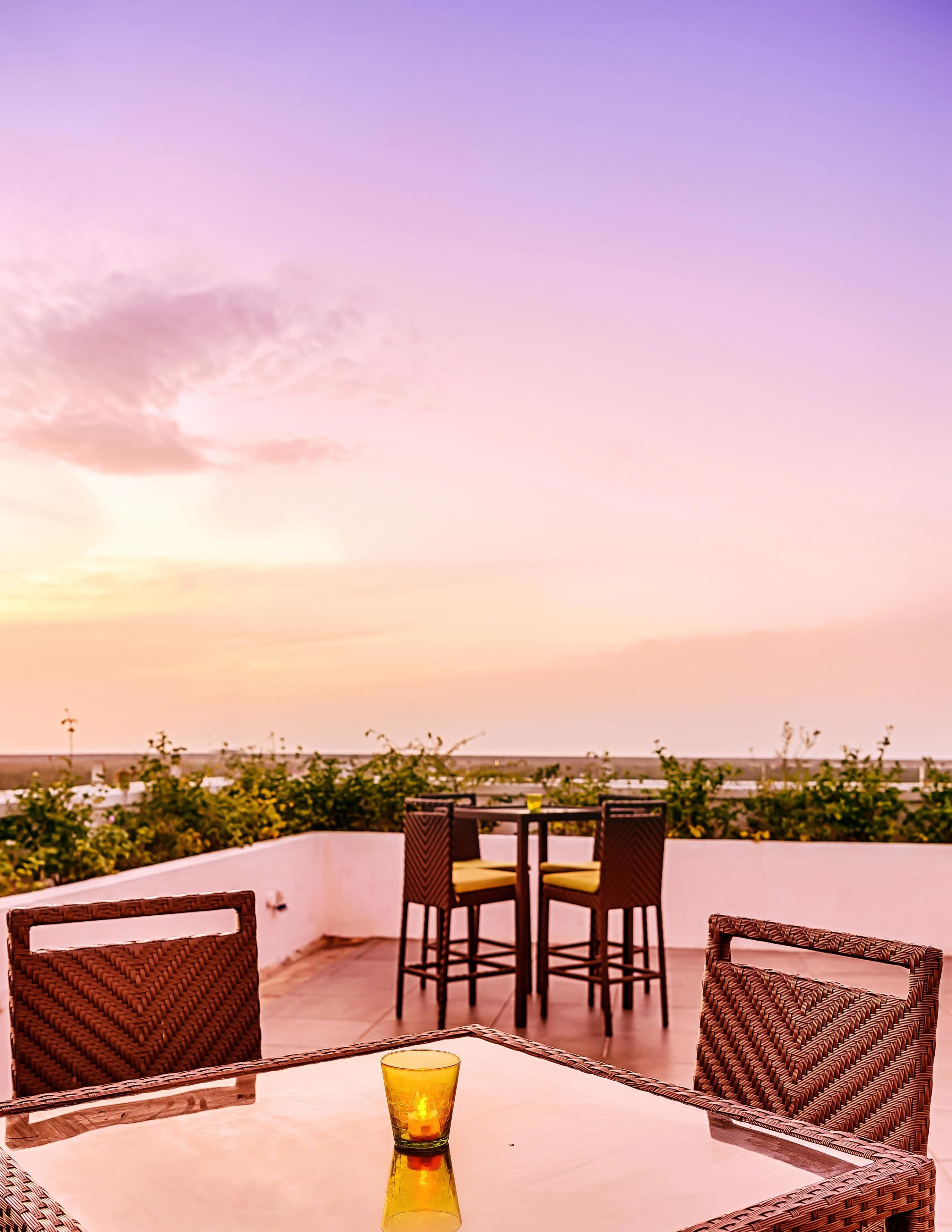 A terrace with wicker furniture and a glass table, overlooking a cityscape.