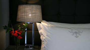 Een nachtkastje met een lamp, een vaas met rode bloemen en een wit kussen met een bloemendessin.