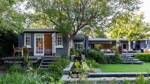 A modern house with a covered patio, outdoor seating, and a small garden. - In Abundance Guest House (Montagu)