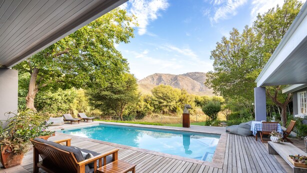 A wooden deck with a pool, lounge chairs, and a table. - In Abundance Guest House (Montagu)