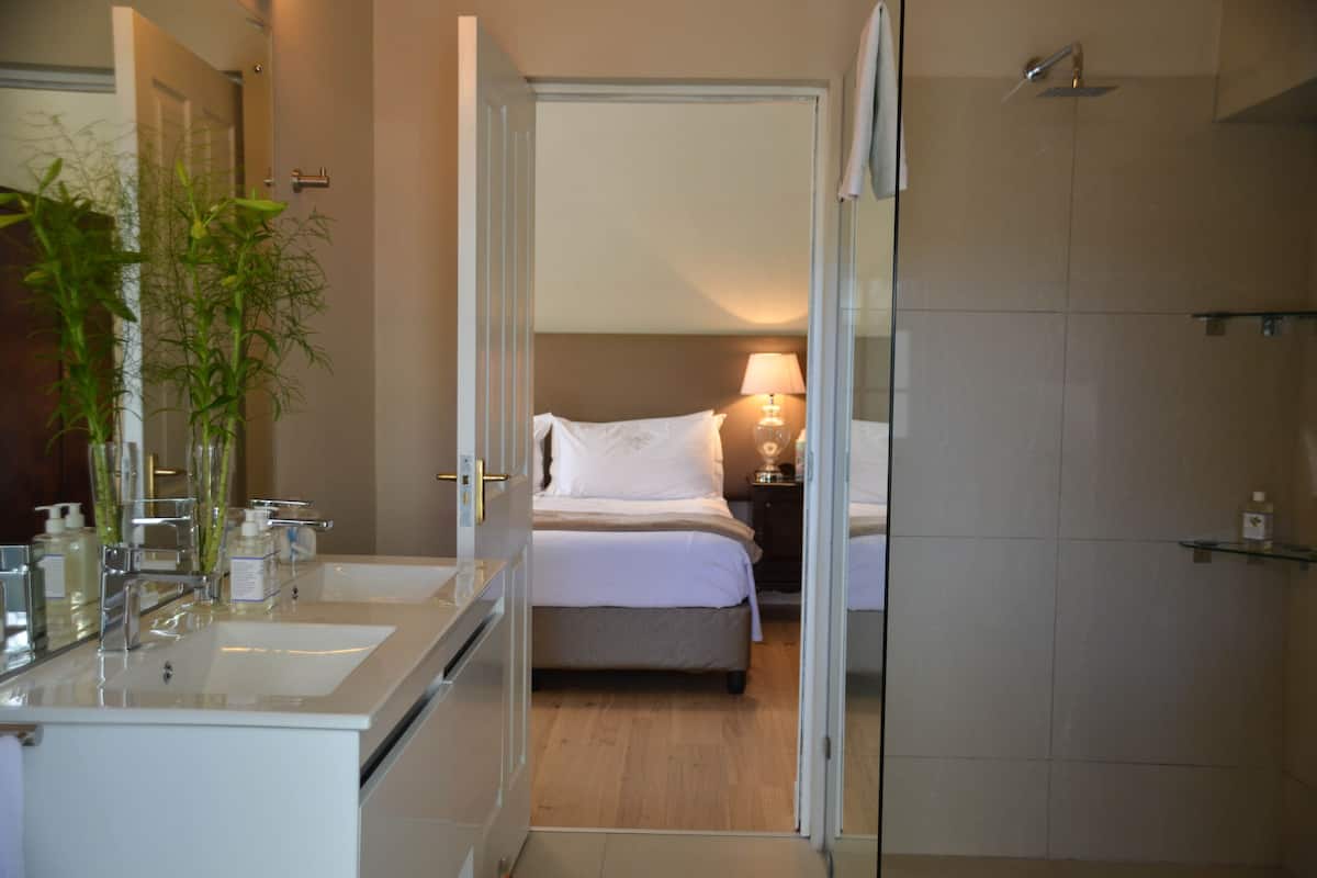 A hotel bathroom with a double sink, a mirror, and a shower area.