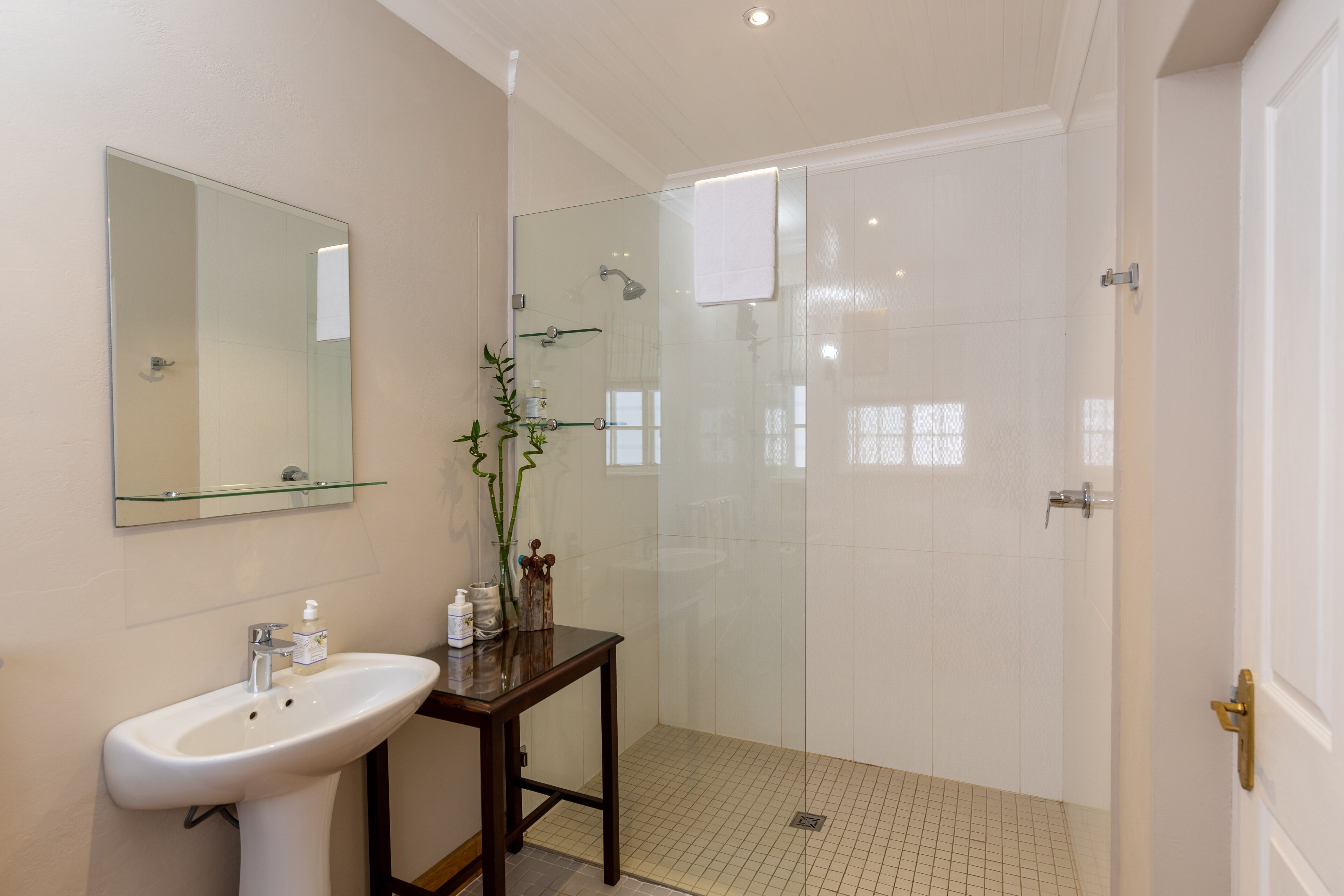 A bathroom with a glass shower enclosure, a sink with a mirror, and a small table with toiletries.