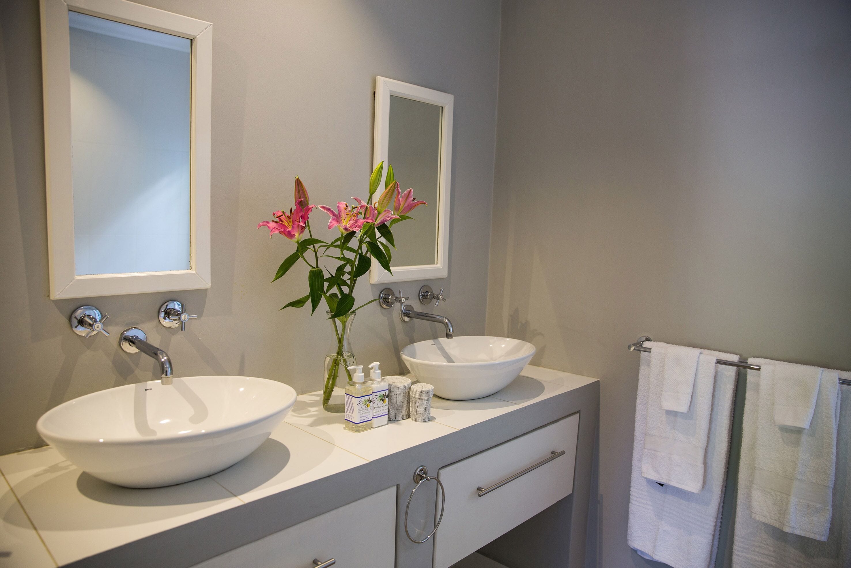 A modern bathroom with two sinks, a mirror, and a vase with flowers.
