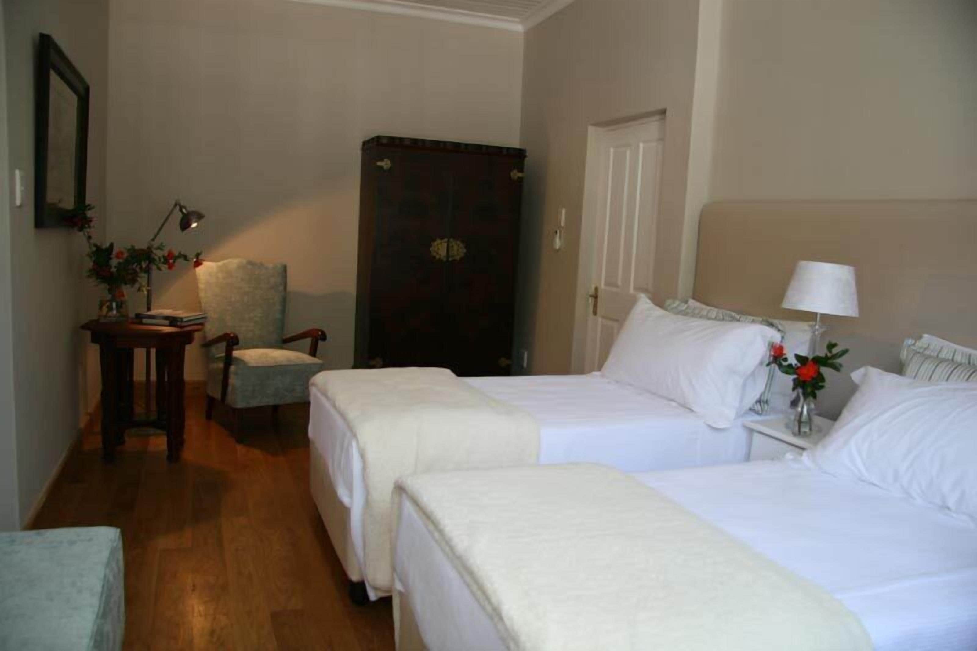 A hotel room with two beds, a chair, a desk, a lamp, and a wardrobe.