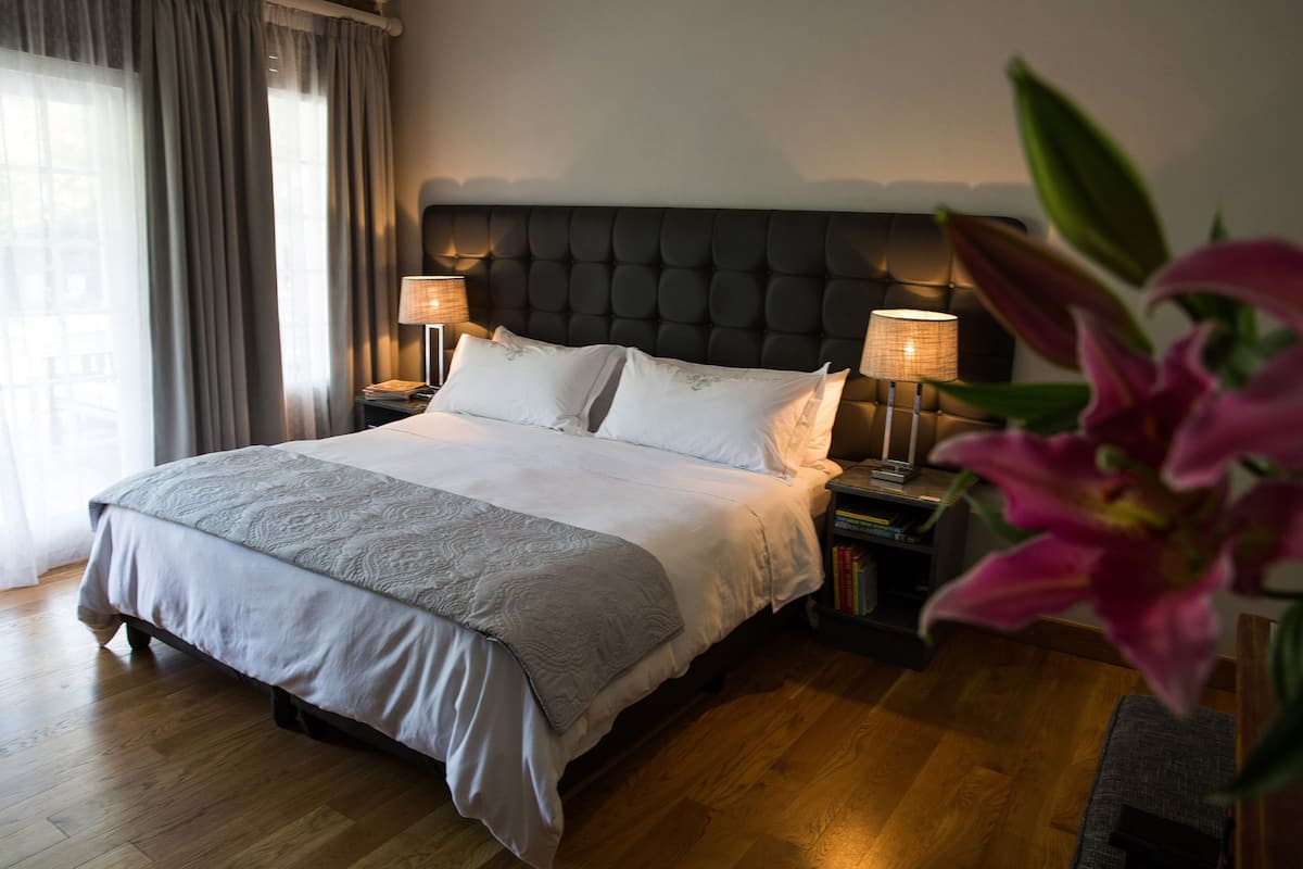 A neatly made bed with a grey and white duvet, two bedside lamps, and a bookshelf with books.