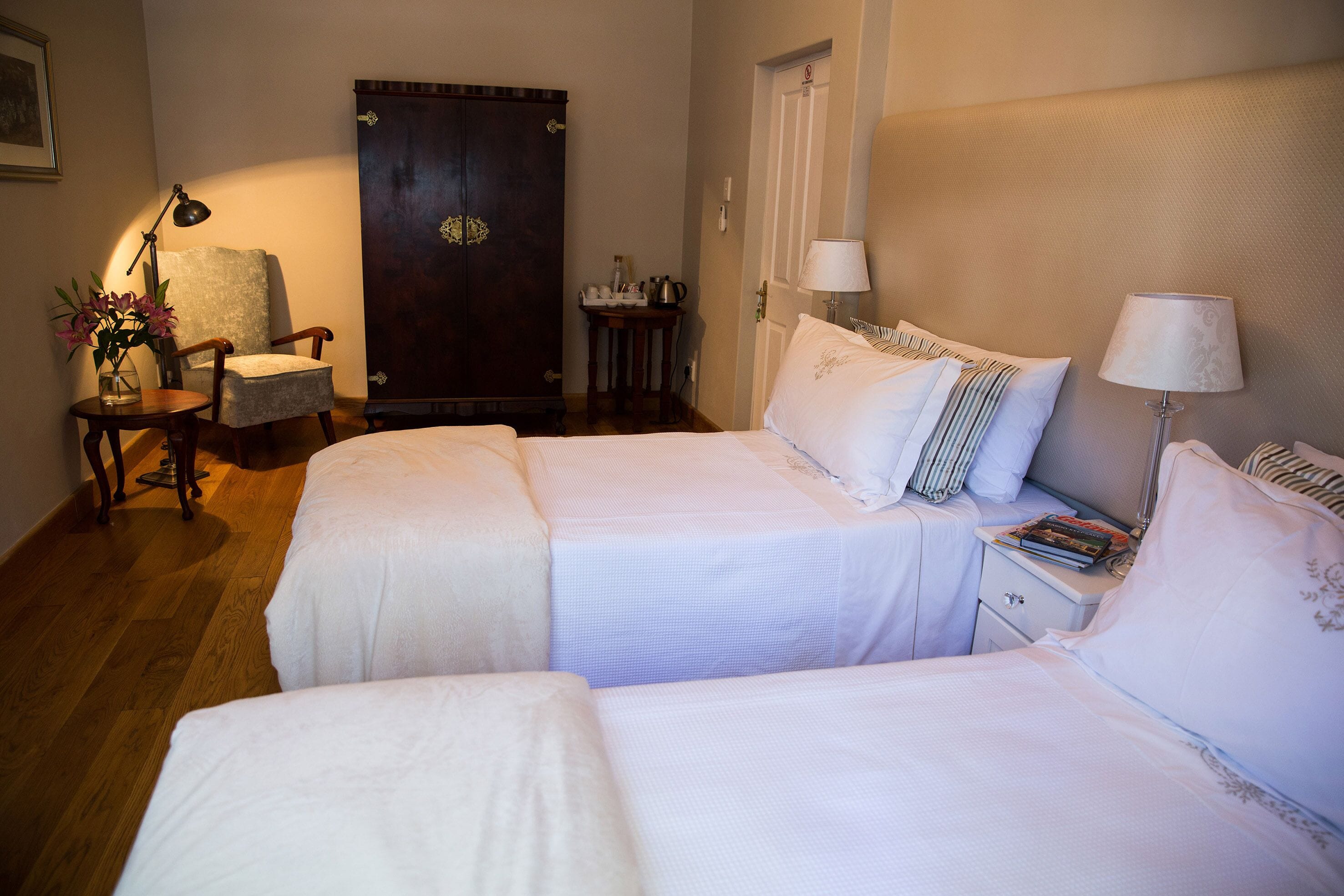 A hotel room with two beds, a desk, a chair, a wardrobe, and a door.