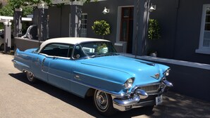 A classic blue car parked in front of a modern house with a white porch and potted plants. - In Abundance Guest House (Montagu)