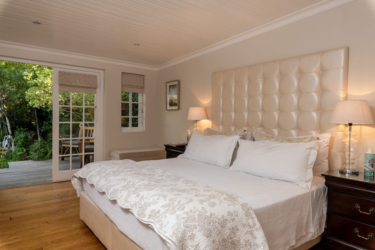 A bedroom with a large bed, wooden floor, and a view of a garden through a sliding door.