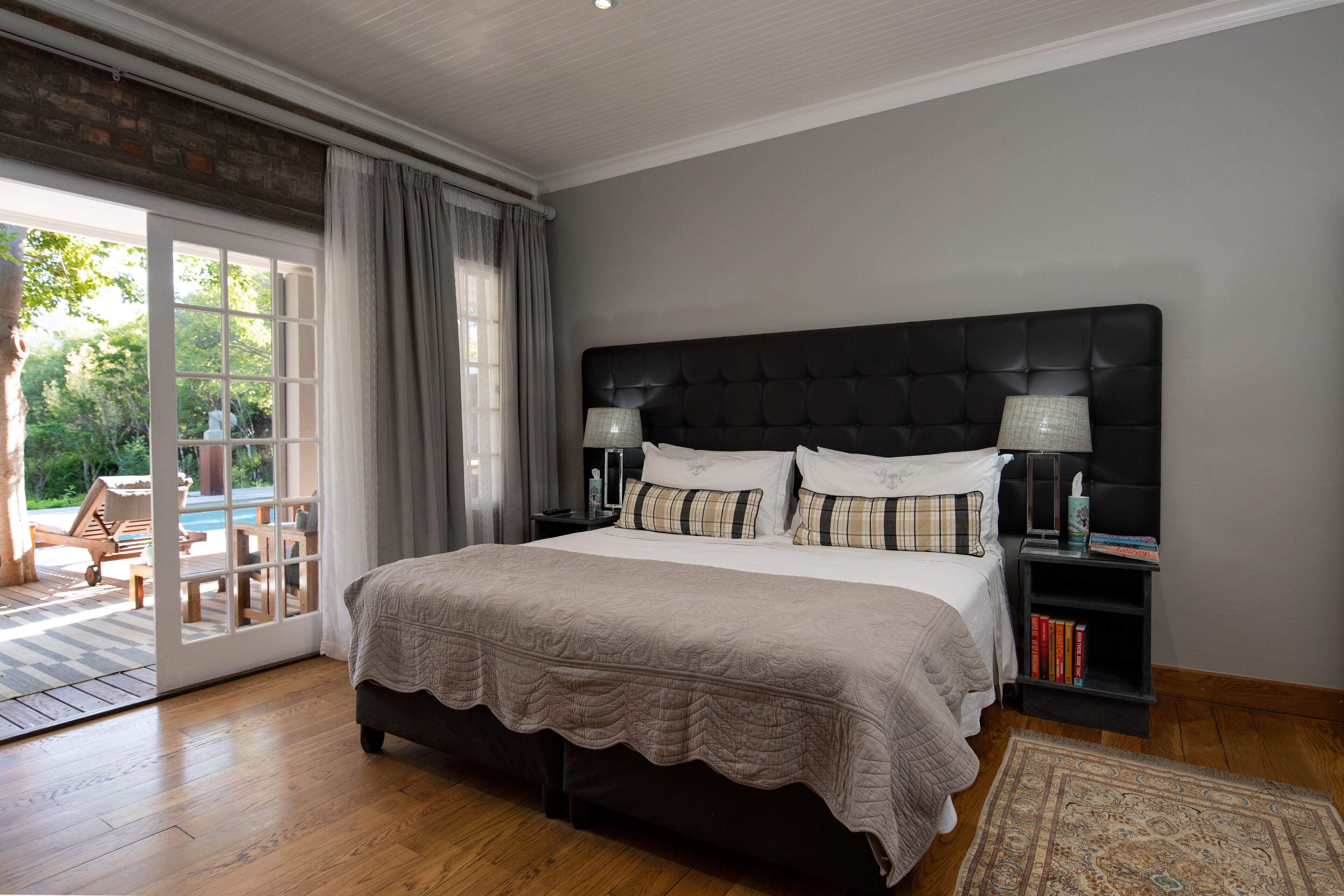Un dormitorio con una cama grande, una mesita de noche, una lámpara y vistas a una piscina y una zona de estar exterior.