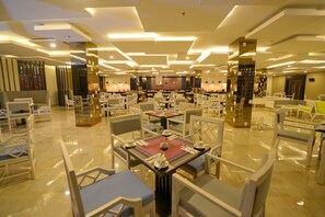 A spacious restaurant with multiple tables and chairs, modern ceiling design, and a polished floor.