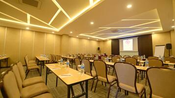 A conference room with multiple tables and chairs, equipped with water bottles and presentation screens.