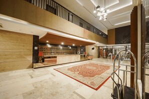 A hotel lobby with a reception desk, a large patterned rug, a staircase, and a modern chandelier.